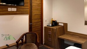 A hotel room with a wooden desk, a chair, a television mounted on the wall, and a small kitchenette area. - The Croft Bnb (Shimla)