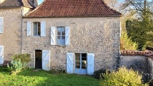 Una casa de piedra con techo de tejas, contraventanas blancas y un césped bien cuidado.