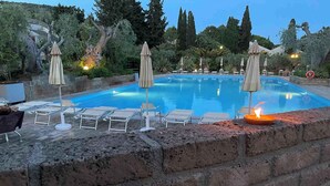 A swimming pool with lounge chairs and umbrellas, surrounded by a brick wall and greenery. - Holiday flat studio apartment with air conditioning (Castiglione della Pescaia)