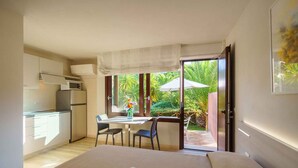 A bedroom with a large bed, a small kitchenette, and a sliding glass door leading to a patio with a table and chairs. - Holiday flat studio apartment with air conditioning (Castiglione della Pescaia)