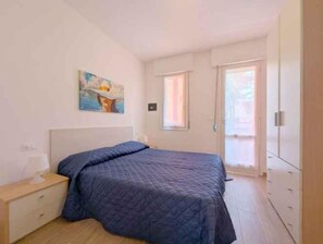 A bedroom with a bed, a nightstand, a painting on the wall, a window, and a door leading to a balcony. - Holiday apartment with air conditioning and terrace with pool view (Bibione)
