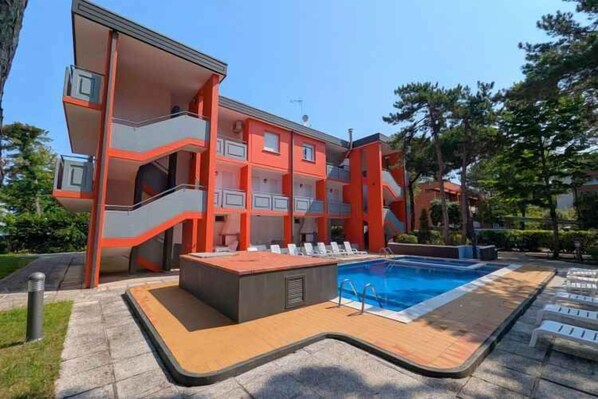 A multi-story building with balconies and a swimming pool area with sun loungers. - Holiday apartment with air conditioning and terrace with pool view (Bibione)