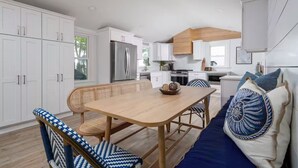 A modern kitchen with white cabinetry, a stainless steel refrigerator, and a dining area with a wooden table and blue and white patterned chairs. - SEAJOY-Waterfront Rare Coastal Gem
Pet Friendly-fenced yard-Completely Renovated (Milford)
