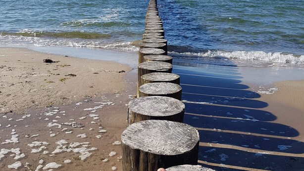 En träbrygga som sträcker sig ut i havet, och på den vilar en persons fötter.
