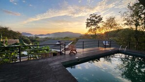Eine Holzterrasse mit Pool, mit Blick auf ein Gewässer und ferne Berge bei Sonnenuntergang.