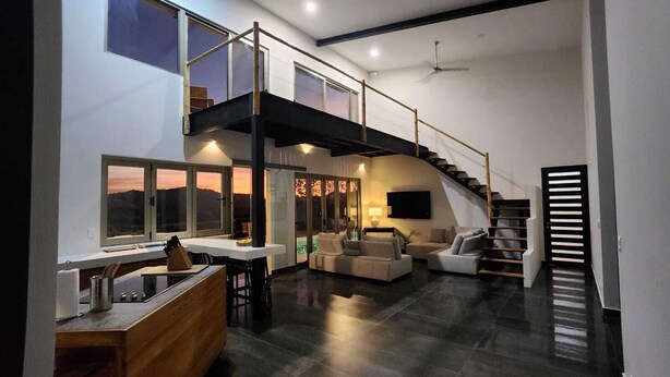 Ein modernes Interieur mit Küche, Essbereich und Wohnbereich, inklusive Treppe und großen Fenstern.