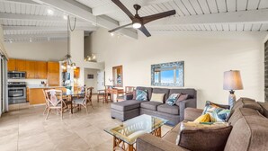 A spacious living area with a sectional sofa, a glass coffee table, and a dining area with wooden chairs and a table. A ceiling fan and pendant lights are visible. - 2 2 Luxurious Wailea Oceanview Resort Vistas (Wailea-Makena)