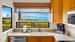 A kitchen with a large window offering a view of a beach and palm trees. - 2 2 Luxurious Wailea Oceanview Resort Vistas (Wailea-Makena)