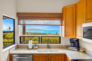A kitchen with a large window offering a view of a beach and palm trees. - 2 2 Luxurious Wailea Oceanview Resort Vistas (Wailea-Makena)
