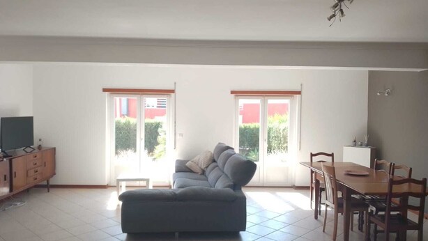 Un salon spacieux avec un canapé gris, une table à manger avec des chaises et un téléviseur posé sur un meuble en bois.