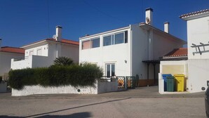 Une maison blanche à deux étages, avec un toit recouvert de tuiles rouges, un petit jardin devant et une antenne parabolique bien visible.