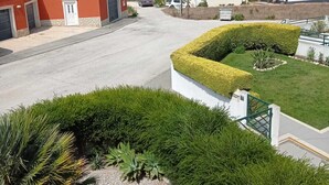 Un quartier résidentiel situé sur la côte, avec des maisons, une route asphaltée et un jardin bien entretenu agrémenté d’une haie et de plantes tropicales.