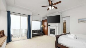 Een hotelkamer met een groot bed, een aan de muur bevestigde televisie, een open haard en een balkon met gordijnen.