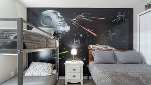 Une chambre avec des lits superposés, une table de chevet avec une lampe et une fresque murale sur le thème de Star Wars.