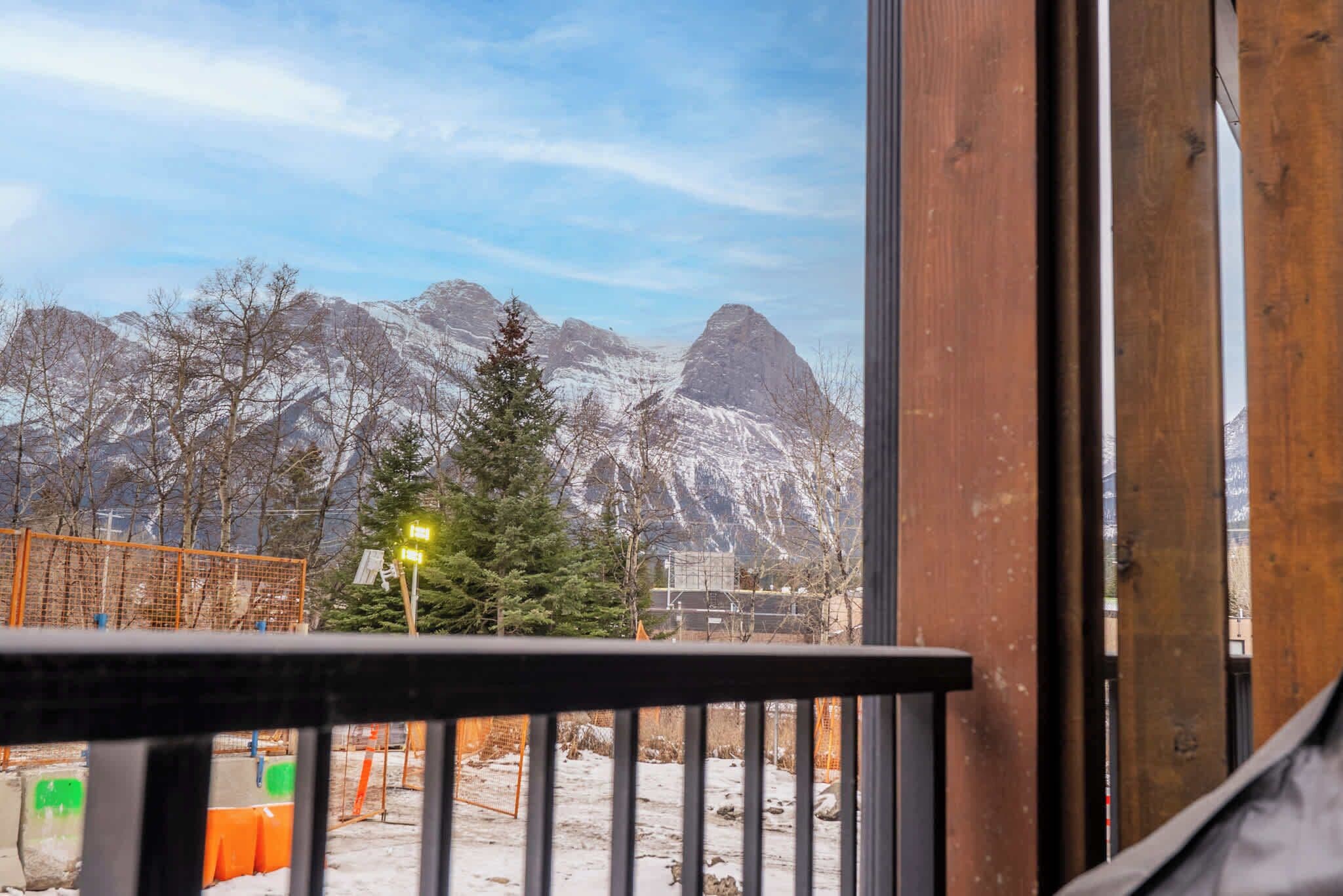 A view from a balcony with a wooden railing, overlooking a snowy mountain landscape with trees and a clear sky.