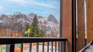 Blick von einem Balkon mit Holzgeländer auf eine verschneite Berglandschaft mit Bäumen und klarem Himmel.