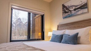 Ein Hotelzimmer mit großem Fenster, einem Bett mit weißer Bettwäsche und einem Gemälde einer Berglandschaft.