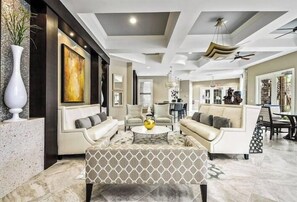 A spacious living room with a sofa set, a coffee table, and a patterned ottoman. - 7545 OS - Solterra Resort Grandeur Luxurious 5-Bedroom Pool Home (Davenport)
