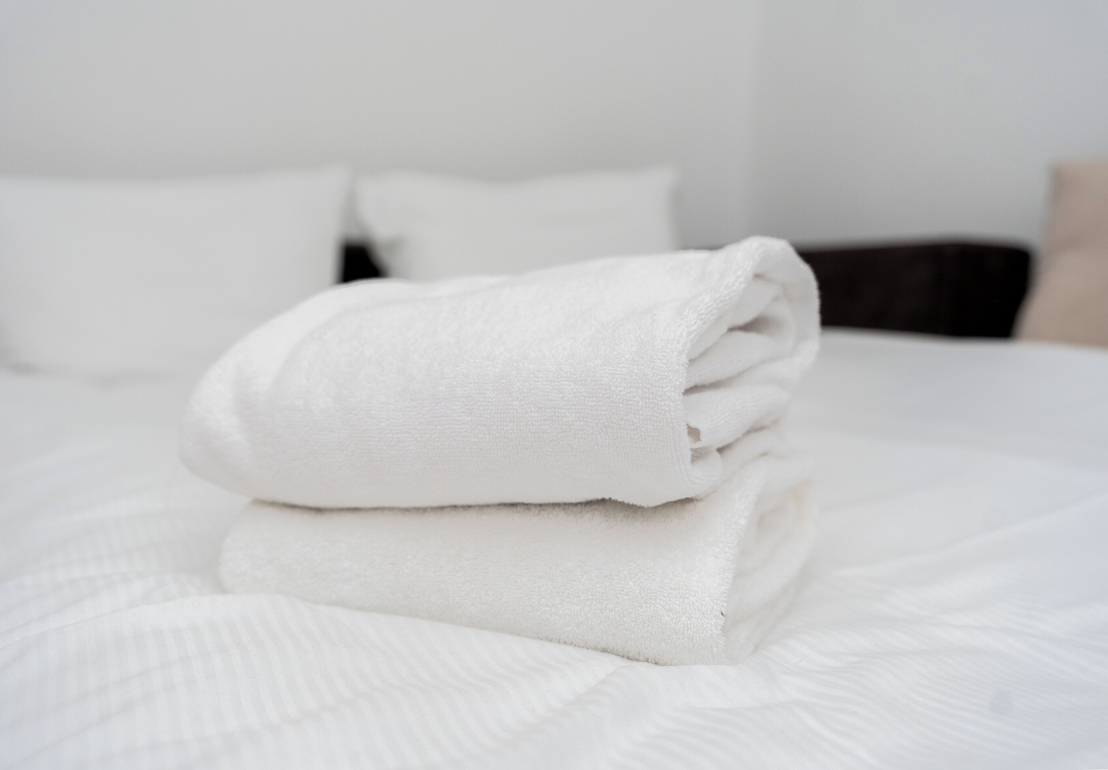Une serviette blanche, soigneusement pliée, est posée sur un lit recouvert d’une couette blanche et de plusieurs oreillers.