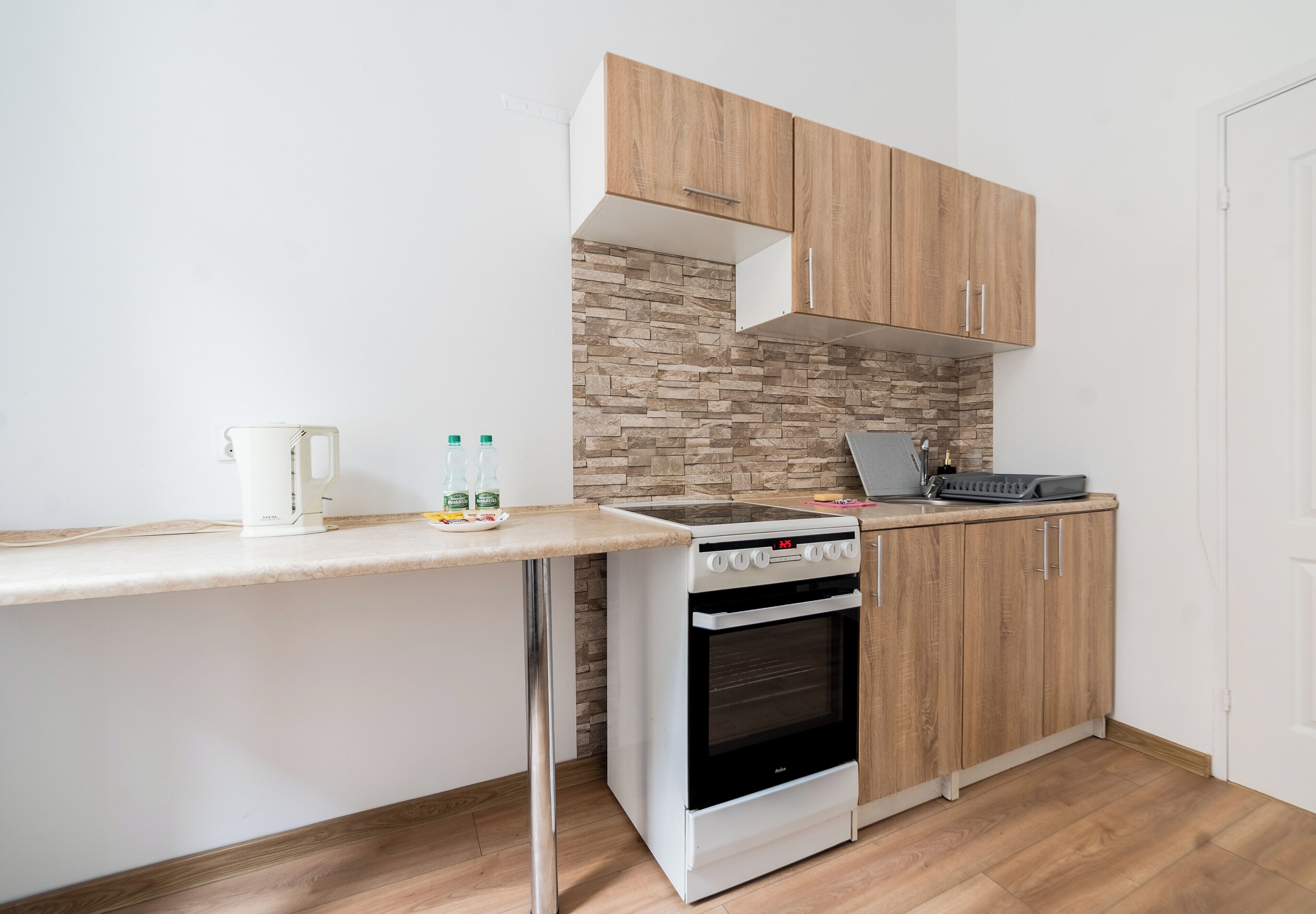 A compact kitchen with a built-in oven, a countertop with a kettle, and wooden cabinets.