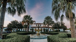 Un cortile con una fontana, palme e un edificio con tetto in tegole.