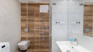 Un bany modern amb dutxa tancada amb vidre, un vàter blanc, un lavabo amb mirall i una rentadora integrada.
