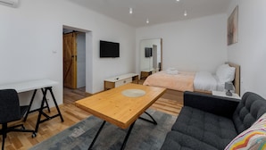 Ett modernt och väl upplyst sovrum med ett skrivbord i trä, en grå soffa, en säng med en vit sänggavel och en platt-TV som är monterad på väggen.