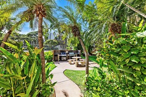 A pathway leading to a barbecue area surrounded by lush tropical vegetation. - Bright and Chic Kihei Condo (Kihei)