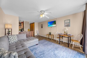 A modern living room with a sofa, a dining table with chairs, a ceiling fan, and a TV mounted on the wall. - Bright and Chic Kihei Condo (Kihei)