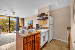 A modern kitchen with a central island, white appliances, and a dining area with a view. - Bright and Chic Kihei Condo (Kihei)