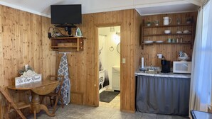 Cocina compacta con paredes de madera, una zona de comedor con el letrero 'Be Our Guest' y una pequeña barra con microondas y cafetera.