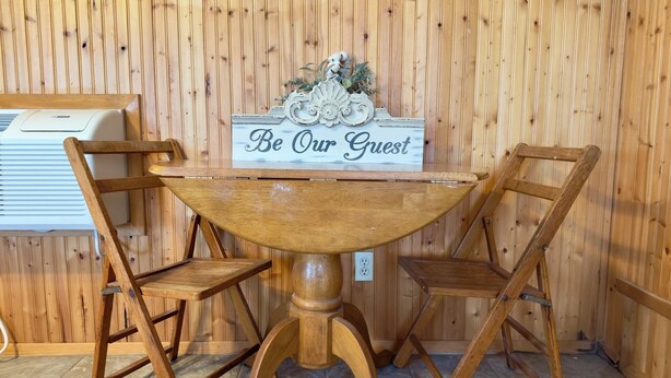 Una mesa de madera con un letrero que dice "Be Our Guest" y dos sillas de madera.
