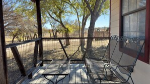 Un patio cubierto con bancos de metal y una mesa de madera, rodeado de una cerca y árboles.