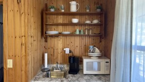 Cocina compacta con paredes de madera, encimera de mármol y equipamiento básico, incluyendo un lavamanos, cafetera y microondas.