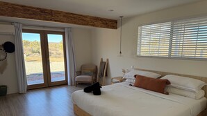 Een slaapkamer met een groot bed, houten vloeren, een schuifdeur naar een terras en uitzicht op de omgeving.