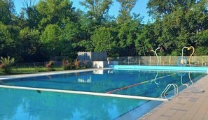 Ein Schwimmbecken mit klarem Wasser, umgeben von einer Backsteindeck und Bäumen.