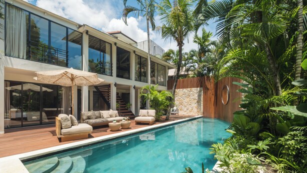 Een modern huis met een zwembad, terras en weelderige beplanting.