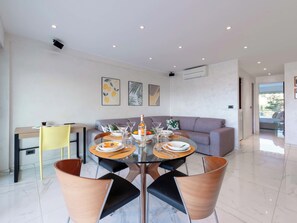 A modern dining area with a round table, chairs, and a sofa in the background. - 1-Br Apartment with Terrace, Near City Centre (Cannes)