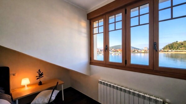 A room with a view of a harbor, a table with a lamp, and a chair. - Apt Ribadesella Downtown, Ocean View - Buenavista (Ribadesella)