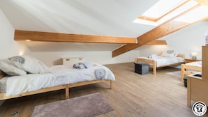 Ett modernt sovrum i en loftvåning med ett sluttande tak, träbjälkar, två sängar, ett litet skrivbord och ett takfönster.