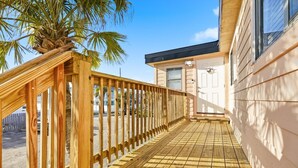 Una terraza de madera con una palmera que conduce a un edificio de fachada blanca y techo negro.