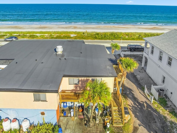 A building with a flat roof, a small patio area with a wooden pergola, and a view of the beach and ocean.