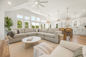 A modern living room with a sectional sofa, a round coffee table, and a dining area with a high table and chairs. - Shorebreak: New Construction, Private Pool, Community Amenities (Corolla)