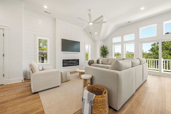 A spacious living room with a large sofa, a television, and a ceiling fan. - Shorebreak: New Construction, Private Pool, Community Amenities (Corolla)