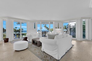 A spacious living room with a white sofa set, a coffee table, and a view of the ocean through large windows. - Naples Beachfront Condo | Stunning Gulf Views | Steps to the Sand (Naples)