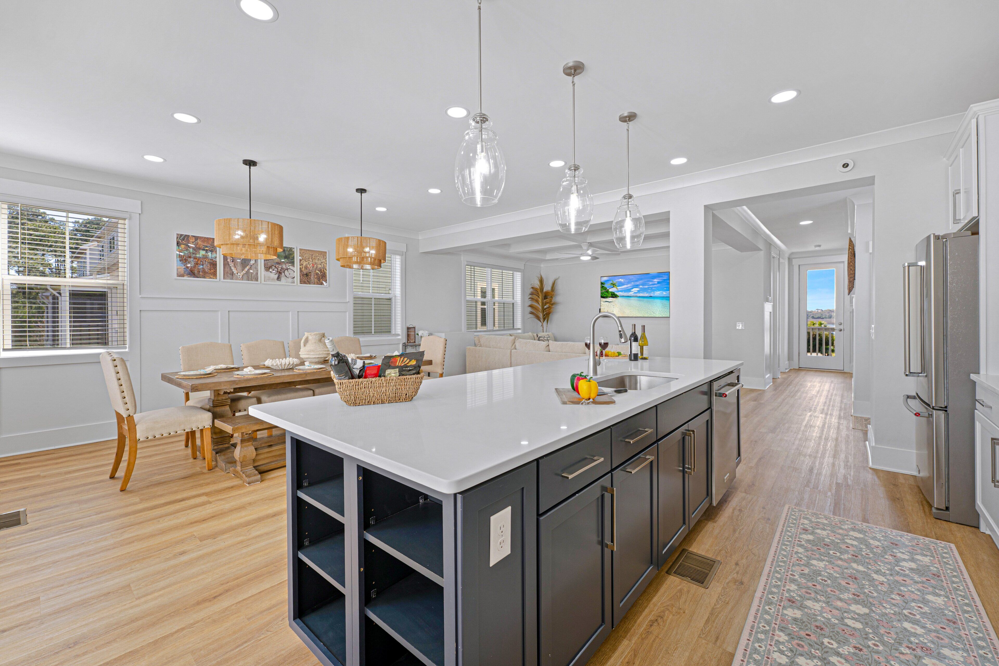 A modern kitchen with a large island, pendant lights, and a view to the outside.