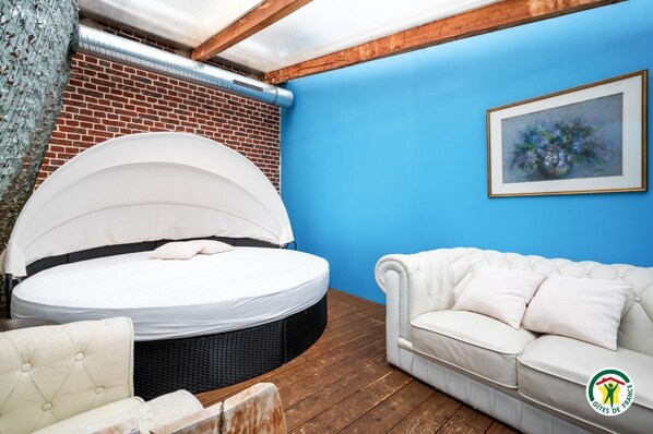 Une chambre avec un lit rond, un canapé blanc et un tableau encadré au mur.