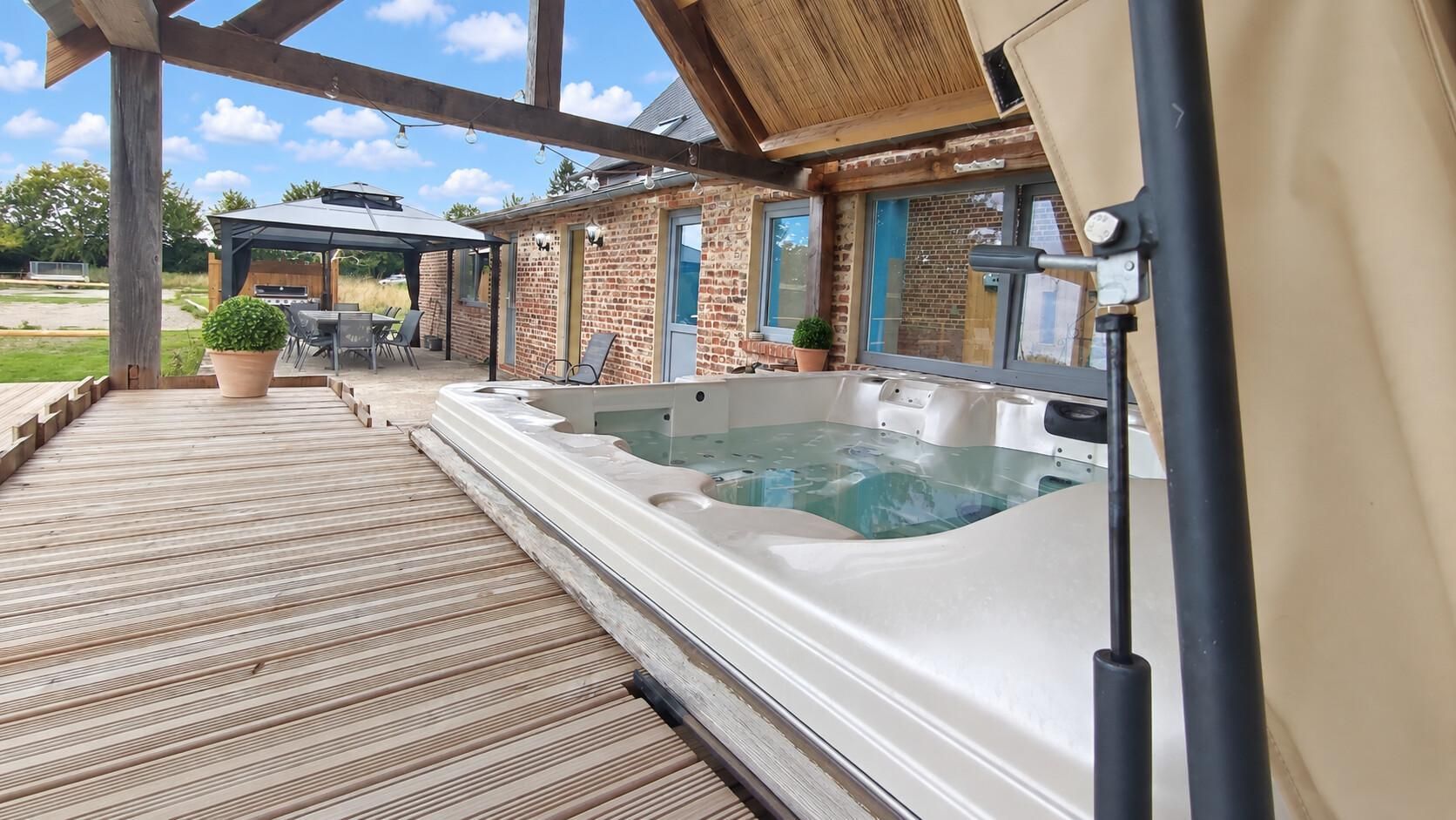 A hot tub under a wooden pergola with a patio area and outdoor furniture.