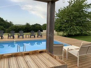 A wooden deck with a pool, Adirondack chairs, and a pergola.