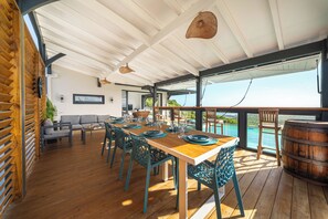 A spacious outdoor dining area with a wooden deck, blue chairs, and a long table set for dining. - Villa Mansfenil - Le Marin- Sea and forest view (Le Marin)